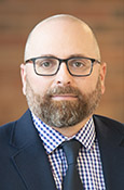 Headshot of Michael Jacobs with glasses and a beard, wearing a suit and tie.