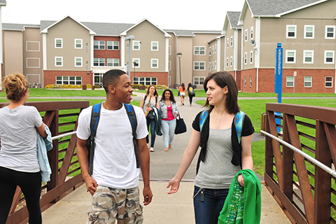 Students walking across the pedestrian bridge between the residence halls and the campus