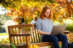 student sitting on park bench working on a laptop