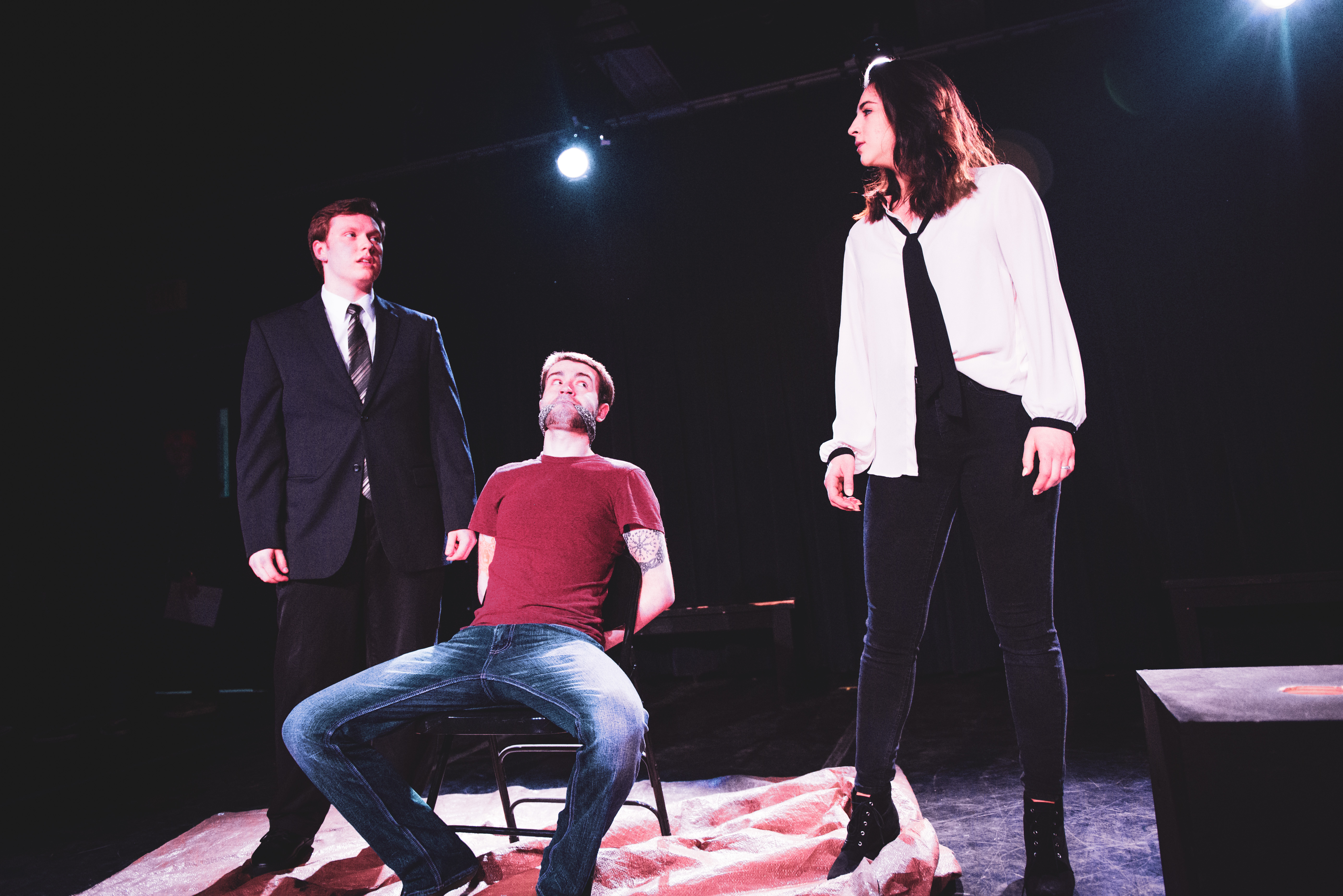 Two theater students standing with 1 theater student wearing a red shirt sitting in a chair in the middle of the two
