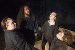 Four Theater students in all black standing in a circle holding hands