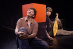 Two male theater students sitting down with their backs agains orange cube
