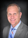 Craig Ross smiling wearing a suit with a colorful plaid patterned tie