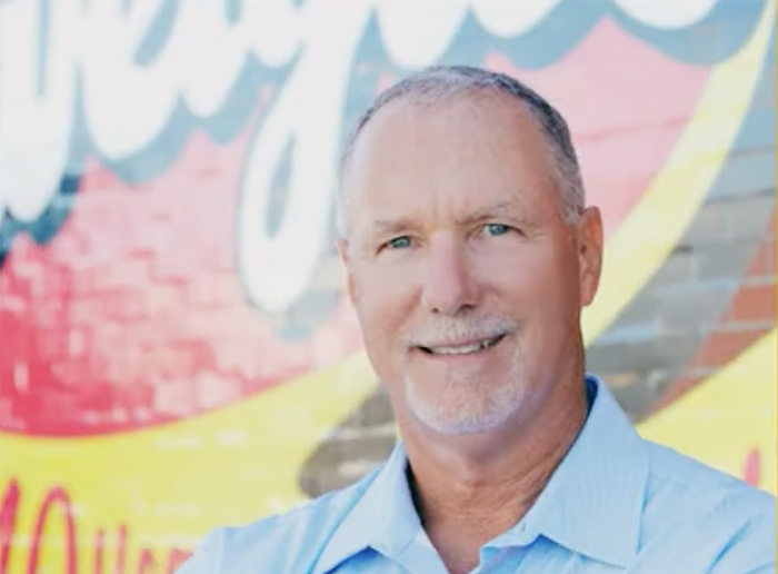 a man smiling in front of a red and yellow "Zweigle's" sign