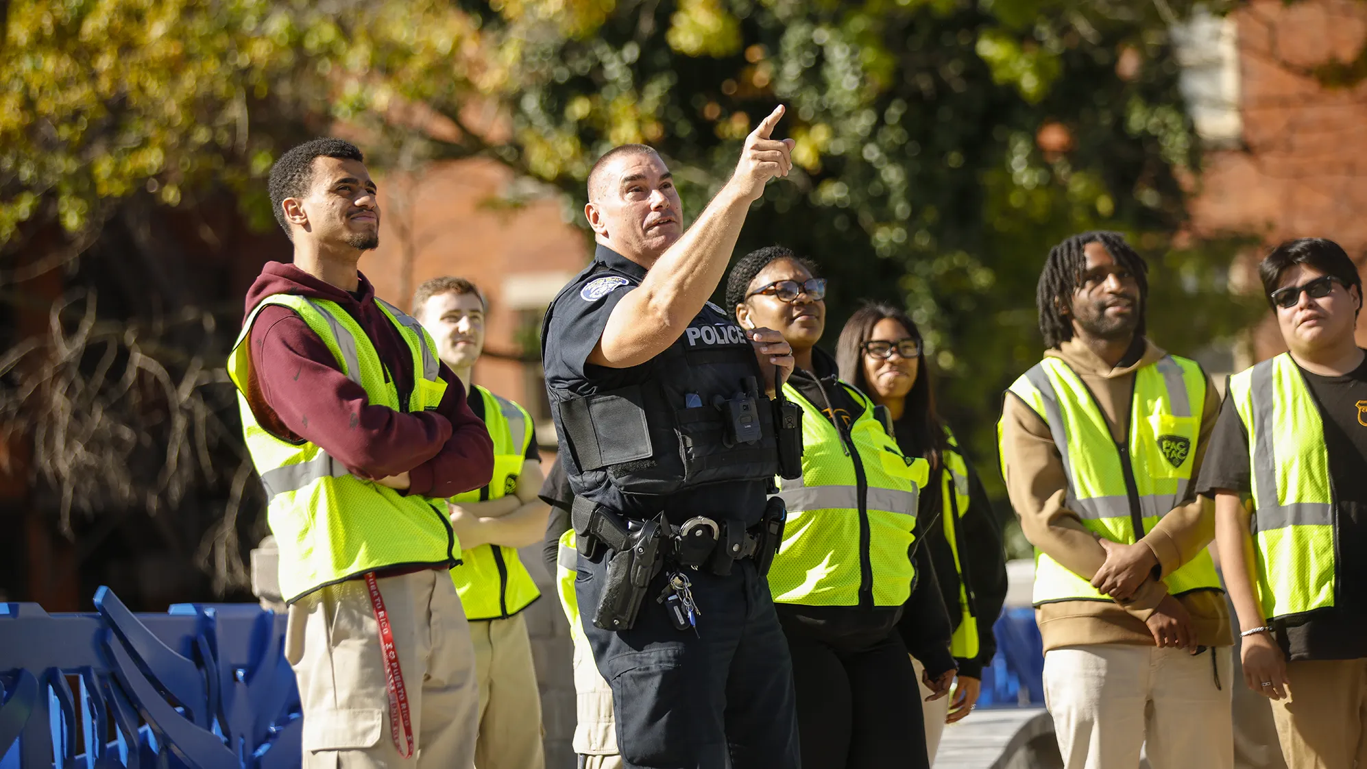 A police officer points upward while surrounded by students