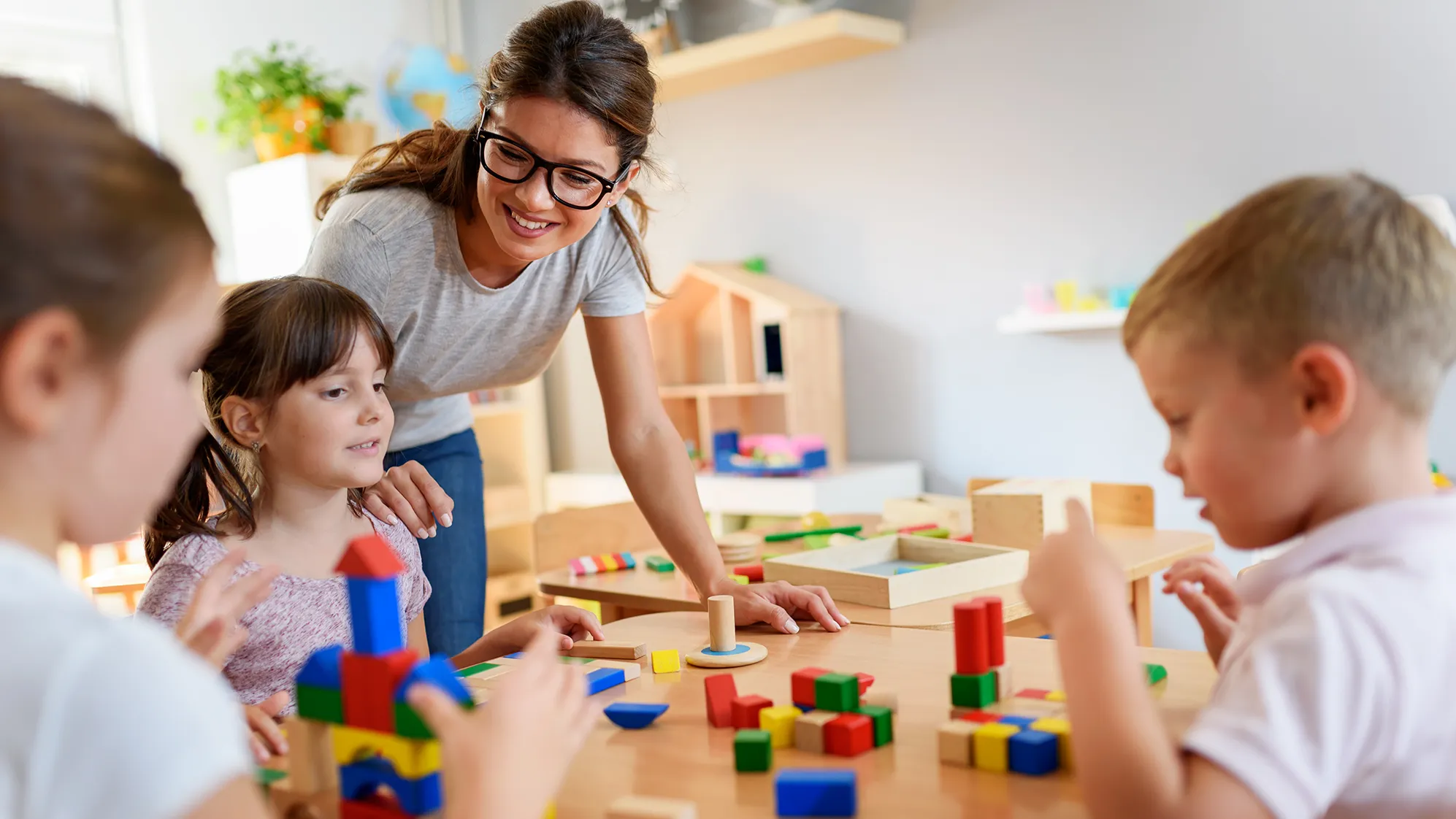 children playing with blocks while a teacher helps