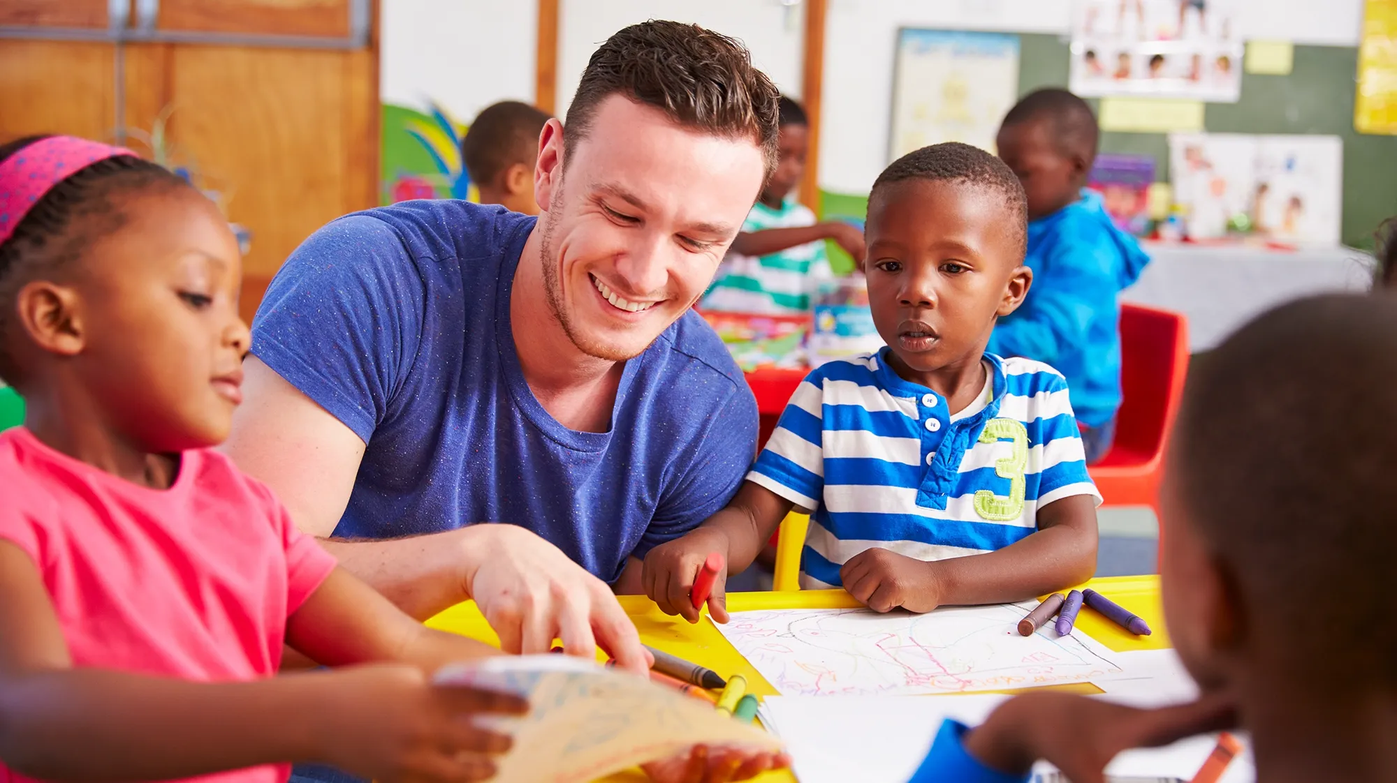 A teacher interacts with children seated around a table
