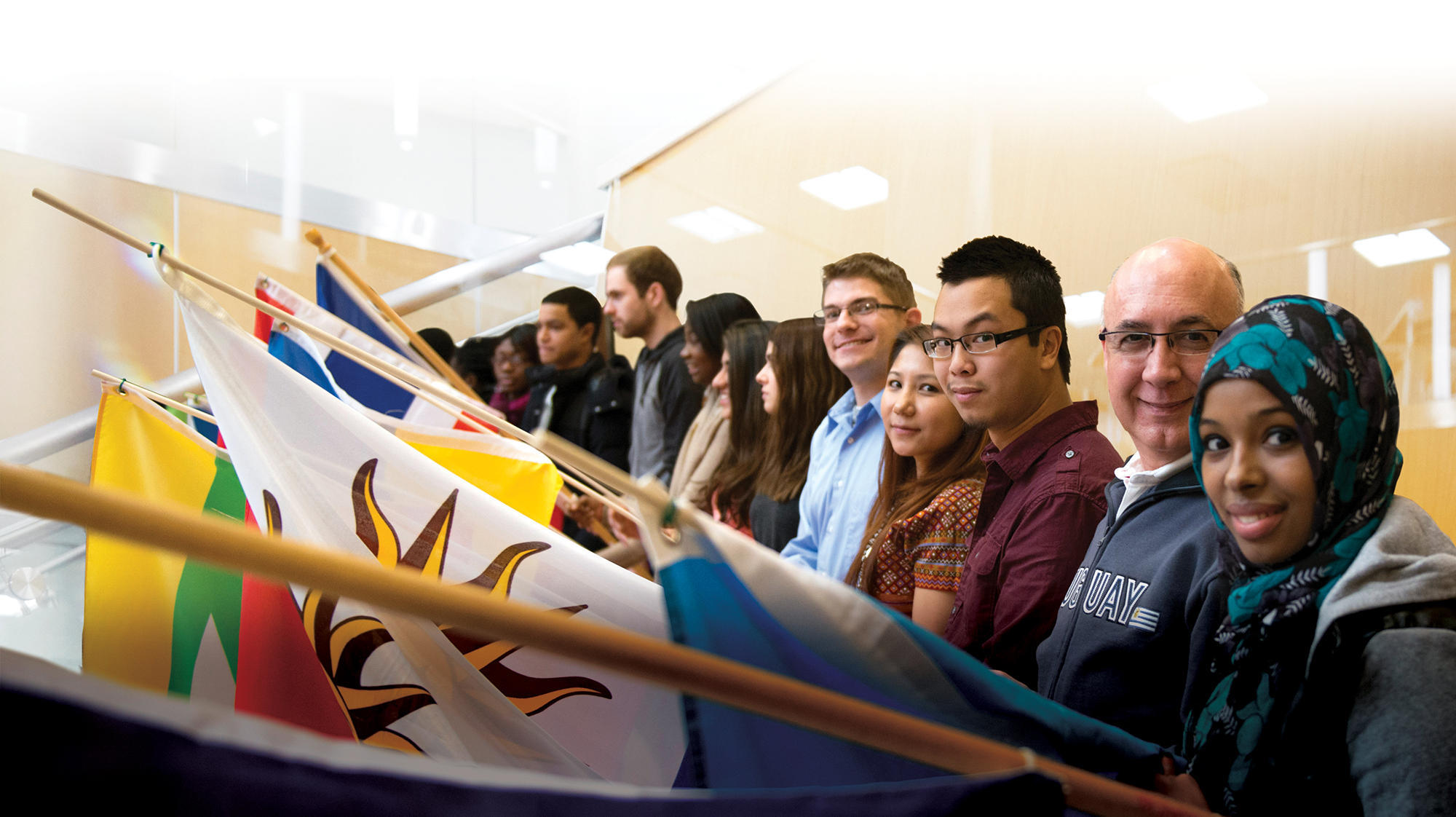 Diverse group of students stands together holding international flags during a multicultural campus event.