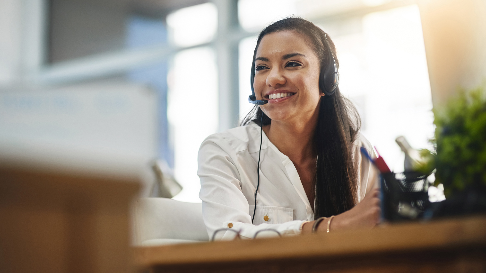 Office administrative assistant wearing a headset smiles while assisting a customer at a desk.