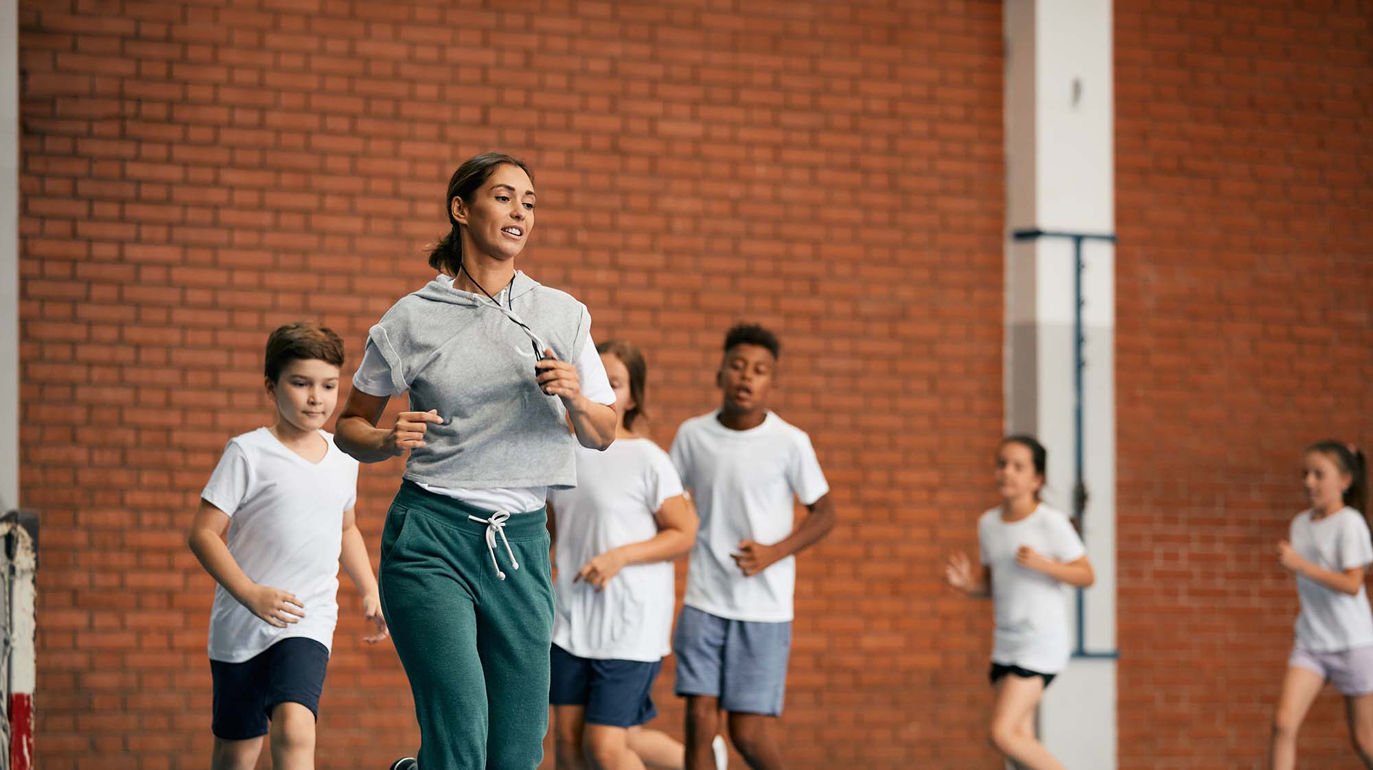 A gym teacher running in a gymnasium with students running behind her
