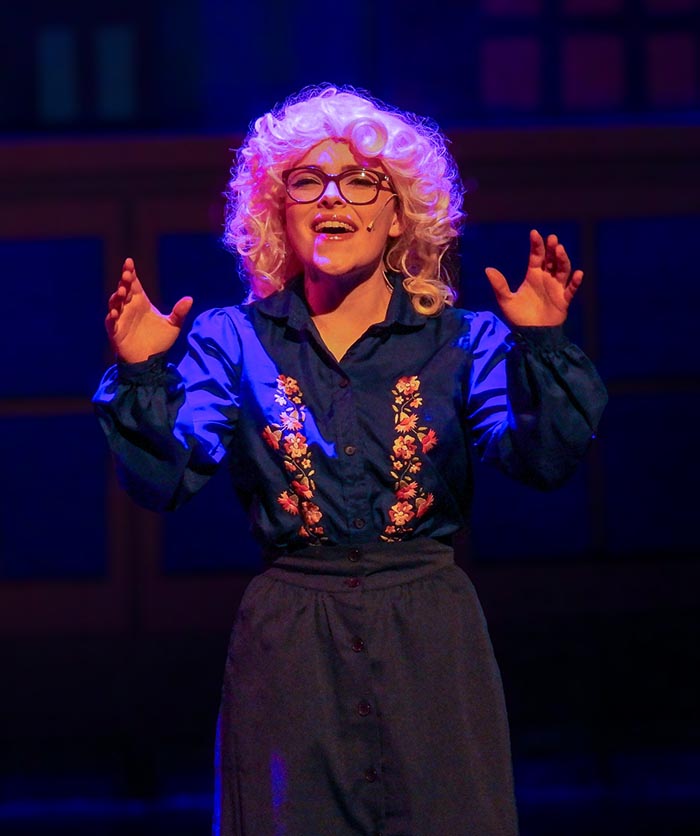 a student in a curly blonde wig and classes performing on stage