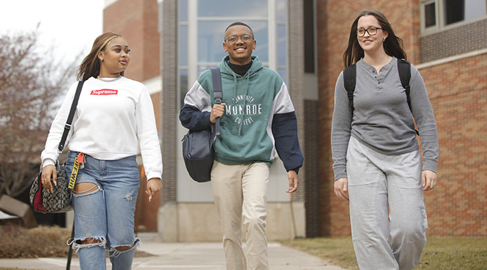 Two female students and one male student walking outside, smiling wearing backpacks