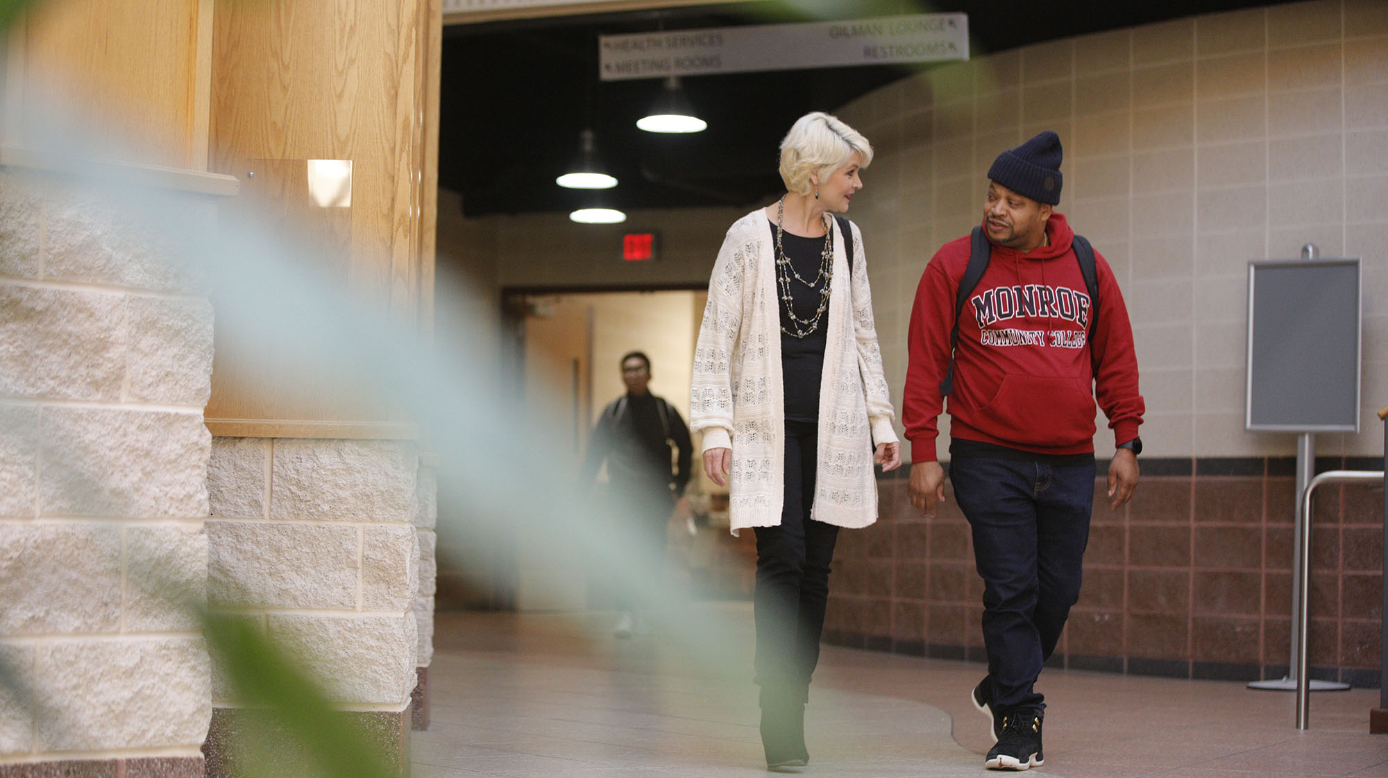 a student in a red sweatshirt walking with a faculty member