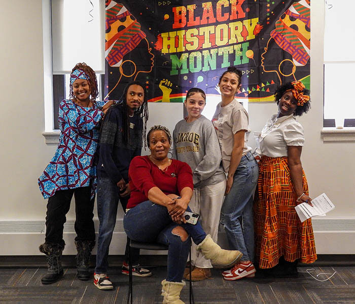 Six people pose together in front of a Black History Month display at Monroe Community College.