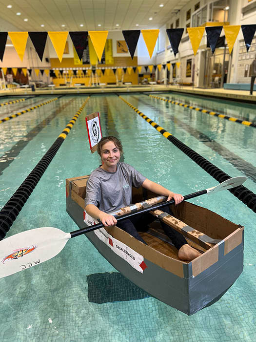 A person participates in a cardboard boat race in an indoor swimming pool.