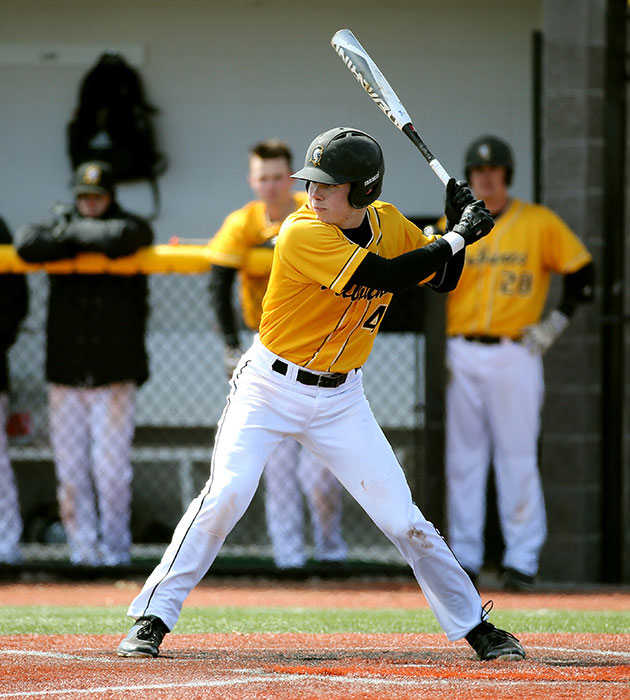 A Monroe Community College baseball player in a yellow uniform and helmet prepares to swing at a pitch during a game.