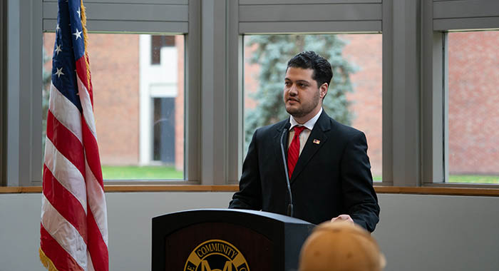 a person giving a speech at a podium with an american flag to their left