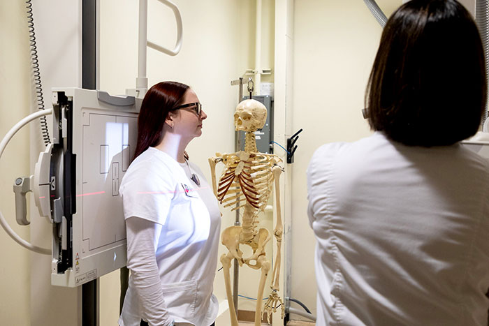 Student standing for a chest x-ray with demonstration skeleton in background