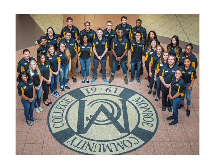 Group photo of MCC Housing & Residence Life team around the MCC crest in the Brighton campus Atrium floor