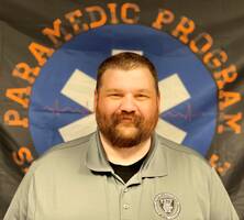 Timothy Hutchings standing in front of a Paramedic Program flag