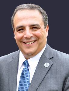 John Rainone wearing a gray suite with a blue tie, smiling