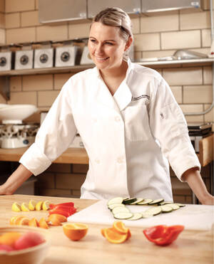 MCC culinary student in chef's jacket standing in front of an array of fresh-cut vegetables in one of the culinary labs
