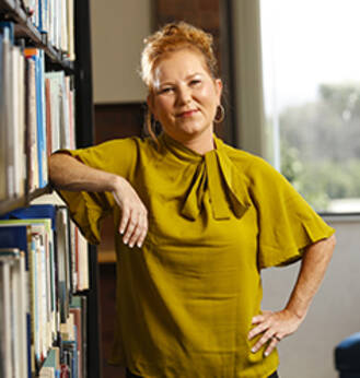 MCC Scholarship/Financial Aid recipient Paula Barlow leaning up against a bookshelf.
