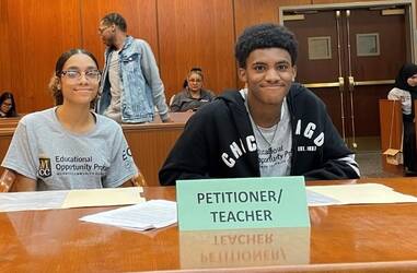 Two EOP students sitting at table for mock trial in court room.