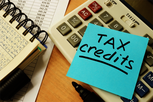 Tax Credit text written on sticky note next to calculator and financial worksheets