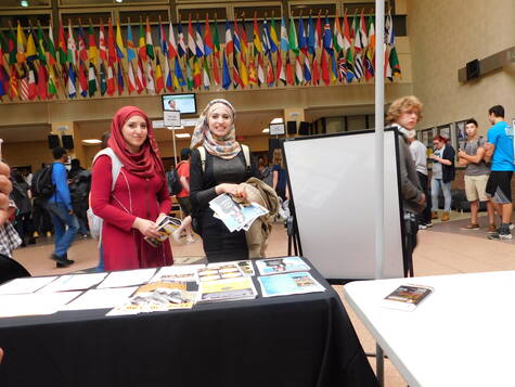 PRISM table set up in the Atrium with students and flags of the world in the background.