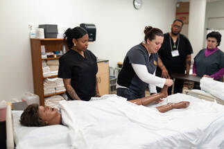 Instructor in Monroe Community College Workforce Development demonstrating a technique to students using a medical training mannequin