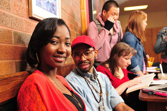 Female and male students smiling while other students meeting in the background