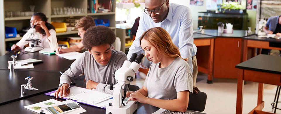 Students with faculty using microscopes in a school lab