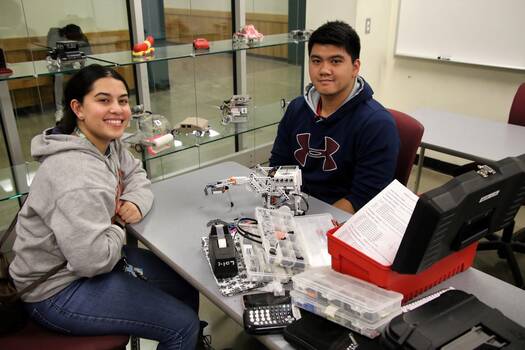 Floor-to-ceiling glass wall allows a view of students working on engineering projects, utilizing updated resources.