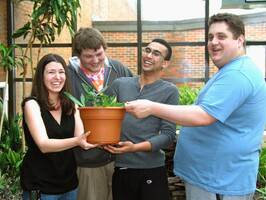 Four MCC students smiling and holding a potted plant