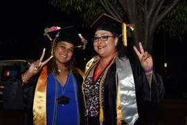 Two female students in graduation cap and gowns holding up fingers in the peace sign gesture