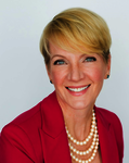 Portrait of Gretchen Wood smiling with short blonde hair, wearing a pink blazer and a 3 layer pearl necklace