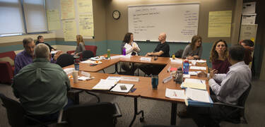 Second year faculty paired off in discussions around a square table.