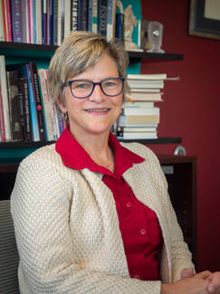 English Professor Kathleen O'Shea, recipient of the American Book Fest's 2021 Best Book Awards honor, seated in front of full bookshelves