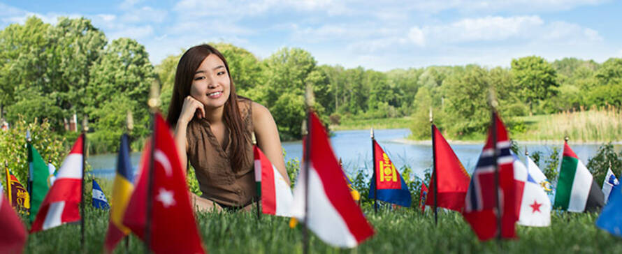 Student sitting in grass near flags.