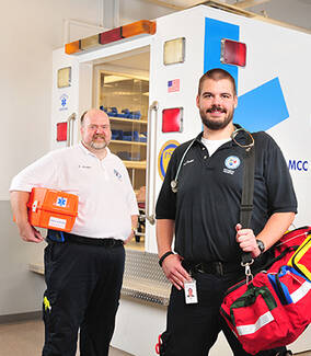 Two male MCC EMS students in front of ambulance simulator at the Public Safety Training Facility in Rochester, NY.